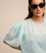 Blusa de chiffon azul marino con cuello redondo, mangas cortas con pliegues en los hombros y textura con felpas.