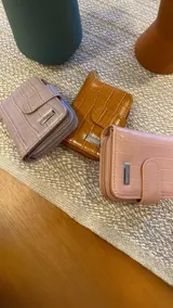 Billetera corta de símil cuero negro con textura de cocodrilo, cierre con presilla y broche a presión, además de compartimento posterior con cremallera.
