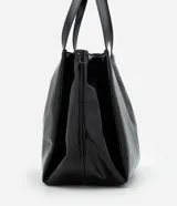 Bolsa tipo shopper de tamaño grande, confeccionada en poliuretano texturizado con acabado brillante. Presenta un diseño estructurado con correas fijas para el hombro, cierre superior mediante botón a presión y un detalle metálico decorativo en la parte frontal.