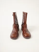 Botas de caña media Mutma modelo Mota, confeccionadas en cuero texturado color marrón. Presentan diseño de punta cuadrada, taco de 5 cm, múltiples tiras con hebillas metálicas ajustables y herrajes circulares en los laterales.