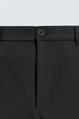 Pantalón de corte regular fit, color negro, confeccionado en tejido elástico. Presenta cintura elástica, cierre frontal con cremallera y botón, bolsillos laterales y bolsillos traseros de vivo.