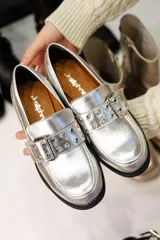 Mocasines plateados de cuero con hebilla y ojalillos.