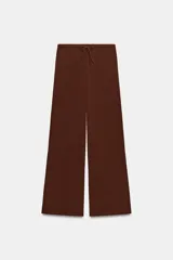 Pantalón palazzo de tiro medio en color marrón, confeccionado en tejido con textura. Cuenta con cintura elástica ajustable mediante cordones y diseño de pierna ancha.