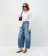 Pantalón de jean estilo barrel con cintura alta, cierre frontal con botón y cremallera, y recortes laterales que definen su silueta amplia y moderna.