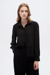 Camisa negra de poliéster con detalles de lurex y textura en relieve, corte holgado, mangas largas con puños y cierre frontal con botones.