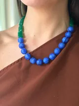 Collar corto de diseño asimétrico compuesto por cuentas esféricas de resina azul con textura grabada y cuentas rectangulares de resina verde. El diseño se completa con un cierre de cadena de acero quirúrgico ajustable.
