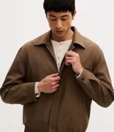 Campera de sarga color marrón, con cuello clásico, cierre frontal con cremallera, bolsillos laterales y cintura con elástico. Diseño de manga larga con corte recto.