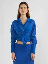 Camisa azul de manga larga con lazo en la cintura y botones nacarados. Confeccionada en 100% algodón con detalle de Polonio en cobre. Hecha en Italia.