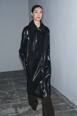 Trench de largo midi con acabado brillante efecto vinilo, manga larga y cuello de solapa en tejido de gamuza a contraste. Presenta cierre frontal con botones ocultos y bolsillos laterales integrados en la costura.