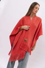Ruana de tejido de punto color coral con flecos en el ruedo y etiqueta de cuero con logo grabado en la parte frontal.