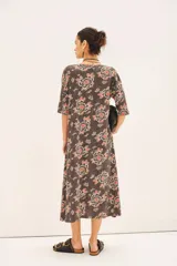 Vestido midi de línea A con mangas 3/4, de caída amplia y tejido liviano. Confeccionado en jersey modal estampado con motivos florales en tonos rojos, blancos y negros sobre un fondo gris oscuro.