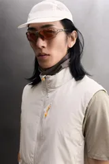 Chaleco técnico de corte regular con cuello subido y cierre frontal de cremallera. Presenta un diseño ligero con panel frontal ligeramente acolchado, bolsillos laterales con cremallera oculta y un bolsillo adicional en el pecho con tirador en color naranja. Incluye acabados con cinta elástica en el bajo y detalle de logo estampado.