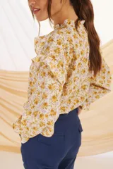 Blusa de manga larga con estampado floral en tonos mostaza y lila, con cuello y puños con volados.