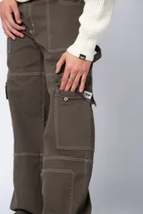Pantalón tipo carpintero de corte relaxed fit y tiro medio, confeccionado en denim negro con costuras a contracolor en blanco. Presenta múltiples bolsillos cargo laterales, un bolsillo con cierre en la parte inferior y presillas utilitarias.