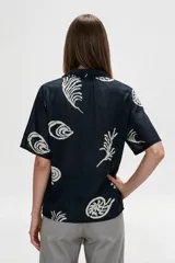 Camisa de algodón con estampado en tonos claros sobre base azul oscura, cuello solapa, mangas cortas y cierre frontal con botones.