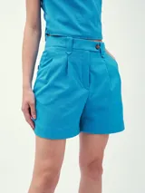 Short de vestir celeste con pinzas delanteras y cierre con botón.