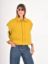 Chaleco puffer corto de color gris, con cuello camisero y cierre frontal oculto. Presenta un diseño holgado y sin mangas.