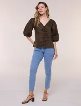 Blusa color beige confeccionada en lino, con escote en V pronunciado y cierre frontal de múltiples lazos para atar. Presenta mangas abullonadas tres cuartos con puños elásticos y corte relajado.