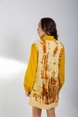 Chaleco de lana merino color crema, con escote en V y diseño sin mangas. Se usa sobre una camisa mostaza de mangas largas con puños elásticos.