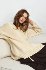 Chaqueta cruzada de punto color beige con manga larga, cuello smoking y cierre frontal con lazada. Presenta detalles de calados en los puños.