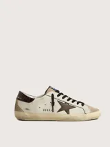 Zapatillas urbanas Golden Goose modelo Super Star, de cuero color blanco con detalles en marrón y beige. Presentan la estrella distintiva de la marca en el lateral, acabado desgastado y suela de goma.