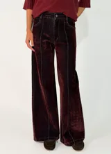 Pantalon de corte recto y tiro medio, confeccionado en denim con acabado aterciopelado en tono marrón oscuro. Presenta costuras verticales marcadas en contraste y cierre frontal con botón y cremallera.