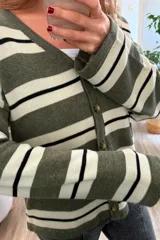 Cárdigan tejido a rayas horizontales en tonos verde militar, blanco y negro, con cuello en V y cierre frontal con botones marrones.