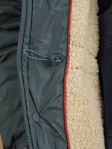 Campera de abrigo azul marino con capucha, cierre frontal con botones y cremallera, múltiples bolsillos y forro interior naranja.