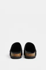 Zueco de símil gamuza color negro, con tachas metálicas plateadas decorativas a lo largo del empeine, plantilla de corcho y suela dentada de goma.