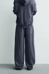 Pantalón jogger de corte wide fit confeccionado en algodón con interior de rizo. Presenta cintura elástica ajustable con cordón, bolsillos laterales y un bolsillo trasero de plastrón. Cuenta con un efecto lavado y acabados irregulares en el ruedo.