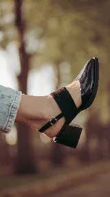 Zapato de taco ancho y medio, color negro, confeccionado en cuero. Presenta diseño destalonado con tira ajustable en el talón, faja ancha de gamuza sobre el empeine y puntera fina de charol.