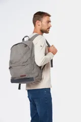 Mochila gris de lona tipo canvas lisa, con base en color gris oscuro. Tiene un bolsillo frontal con cierre y correas ajustables.