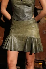 Falda corta de cuero ovino color verde oliva vintage, de tiro medio y diseño con vuelo y volado amplio en el ruedo.
