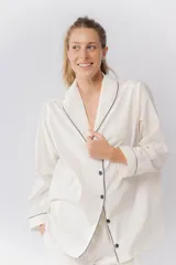 Pijama de dos piezas confeccionado en popelina de algodón. Incluye una camisa de manga larga con cuello smoking, cierre frontal abotonado y detalles de vivo en contraste en cuello, puños y solapas. El pantalón cuenta con cintura elástica, bolsillos laterales y detalles de vivo en los bajos.