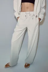 Pantalón de tiro medio color beige, de pierna ancha y corte recto. Cuenta con cintura elástica ajustable con cordones y bolsillos frontales.