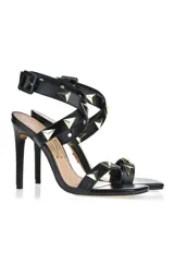 Sandalias de tacón alto color beige con tiras finas y tachas piramidales doradas.