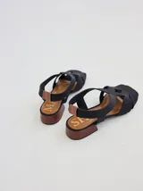 Sandalias bajas negras con tiras anchas de neopreno entrecruzadas en el empeine y talón descubierto. Plataforma de madera con letras grabadas en la plantilla.