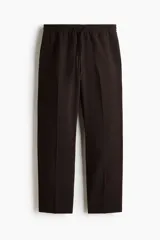 Pantalón relaxed fit color marrón, confeccionado en tejido suave, con cintura elástica ajustable mediante cordón, bolsillos laterales discretos, bolsillo posterior insertado y piernas rectas con pliegues frontales y traseros.