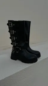 Botas de cuero negras de caña alta con hebillas plateadas y suela track.