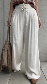Pantalón palazo de lino color beige, de calce amplio y fluido, con tablas en el frente, botón, cierre y cordón ajustable en la cintura.