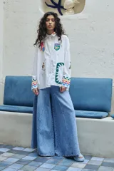 Camisa blanca de corte oversize con bordados de motivos playeros y mangas largas con puños decorados con ondas de colores.
