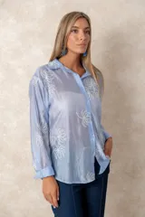 Camisa de manga larga en color blanco, confeccionada en tejido traslúcido con delicados bordados florales en hilo de seda al tono. Presenta cuello clásico, cierre frontal con botones y puños abotonados.