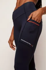 Calza deportiva de tiro alto color negro, confeccionada en poliamida de alta performance. Presenta bolsillos laterales con costuras en color verde neón y detalle de estampado reflectante en la pierna izquierda.