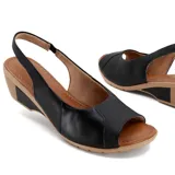 Sandalia de cuero negra con puntera abierta y talón cubierto. Cuenta con una tira trasera con hebilla y una plataforma de goma color beige con tecnología Care Juanetes.