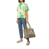 Bolso tote de lona en color beige, con diseño rectangular y estructura rígida. Presenta el nombre del modelo y la marca estampados en la parte frontal en color blanco. Cuenta con doble asa superior, cierre de cremallera en la parte superior y compartimento principal amplio.