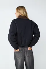 Campera corta de estilo casual, color negro, con cuello de pana en tono contrastante. Presenta cierre frontal con botones a presión, bolsillos laterales, y puños y bajo con acabado elástico.