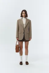 Blazer de lana color beige, con solapas de cuello sastre, cierre frontal de dos botones y bolsillos rectangulares. Presenta un calce relajado tipo overfit y hombreras marcadas.