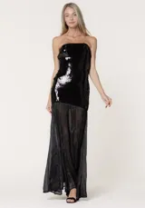 Vestido largo de fiesta con escote strapless. La parte superior presenta un diseño ajustado cubierto de lentejuelas negras, mientras que la parte inferior está confeccionada en chiffon plisado con paneles godet que aportan volumen y movimiento.