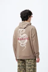 Canguro marrón con capucha, bolsillo frontal y puños ajustados. Estampa frontal con la palabra 'Dramatic' y gráfico en la espalda con tipografía bold y serpiente ilustrada.