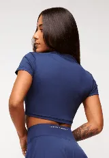 Top cropped azul marino con cuello polo y mangas cortas. Presenta un logo estampado en el pecho.